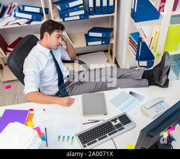 Businessman travaillant dans le bureau avec des piles de livres et papiers doing paperwork Banque D'Images