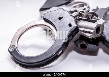 Un ensemble de deux tons de menottes en métal sur le dessus de deux revolvers, une noire et l'autre l'acier inoxydable sur un fond blanc Banque D'Images