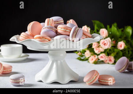 Close-up de macarons sur un stand de gâteau blanc. beau bouquet de roses et une tasse de café à l'arrière-plan noir, l'espace libre Banque D'Images