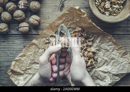 L'homme serre les noix avec nut cracker sur table en bois. Banque D'Images