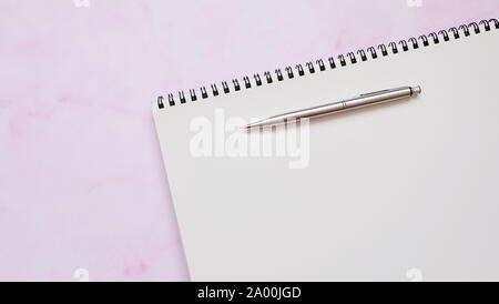 Un carnet de croquis en spirale avec un portemine, sur une surface rose. Banque D'Images