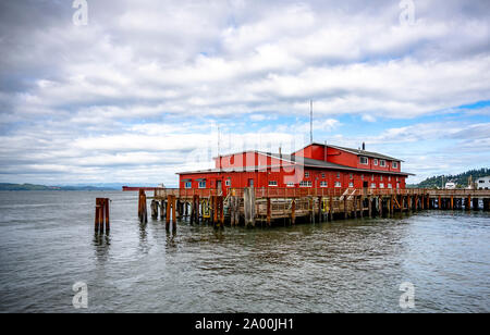 Bâtiments en bois commercial rouge d'un ancien pilote de pêche et de pier avec pieux métalliques qui dépassent de l'eau à l'échelle de l'embouchure du fleuve Columbia dans Banque D'Images