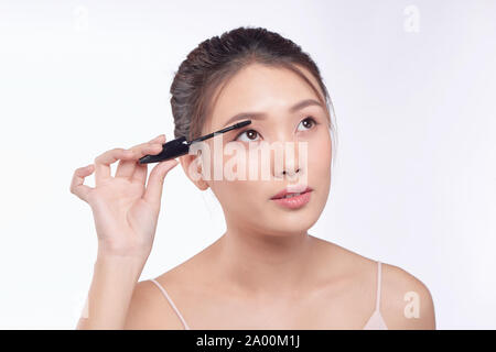 Woman putting Mascara maquillage sur les yeux. Modèle féminin asiatique face closeup oeil avec la brosse sur les cils. Banque D'Images