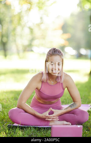 Jeune belle fit woman sitting on the grass on exercise mat looking at tablet pc et souriant elle tenue à l'extérieur de la formation en ligne Banque D'Images
