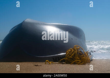 Bateau chaviré sur la plage de sable. Du beau temps et de petites vagues Banque D'Images