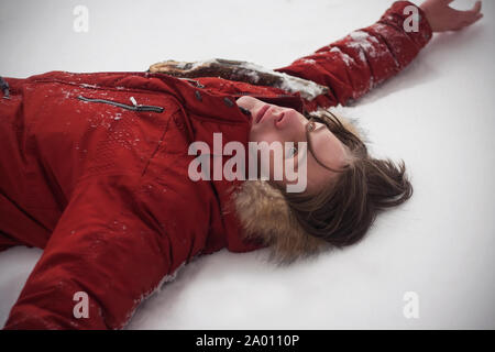 Voyager guy dans une veste rouge se trouvant sur la surface d'un banc de neige dans l'hiver froid avec un regard vide. Banque D'Images