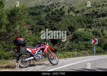 Une moto enduro rouge sur le côté gauche de la route, la forêt est à l'arrière-plan et se tient sur la masse d'asphalte Banque D'Images