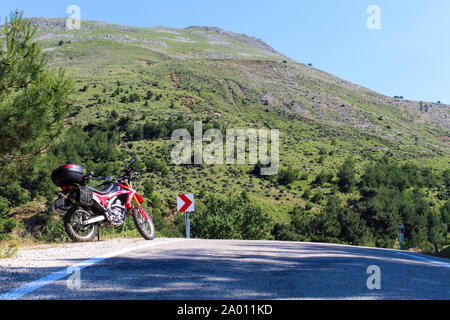 Une moto enduro rouge sur le côté gauche de la route, la forêt est à l'arrière-plan et se tient sur la masse d'asphalte Banque D'Images