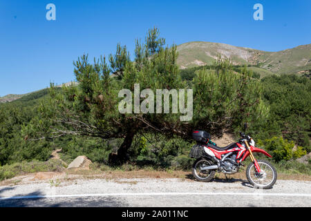 Une moto enduro rouge sur le côté gauche de la route, la forêt est à l'arrière-plan et se tient sur la masse d'asphalte Banque D'Images