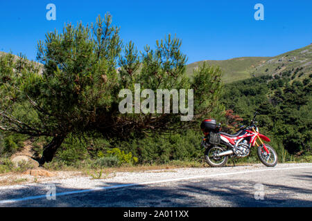 Une moto enduro rouge sur le côté gauche de la route, la forêt est à l'arrière-plan et se tient sur la masse d'asphalte Banque D'Images