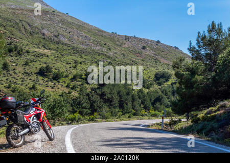 Une moto enduro rouge sur le côté gauche de la route, la forêt est à l'arrière-plan et se tient sur la masse d'asphalte Banque D'Images