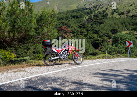 Une moto enduro rouge sur le côté gauche de la route, la forêt est à l'arrière-plan et se tient sur la masse d'asphalte Banque D'Images