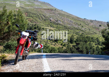 Une moto enduro rouge sur le côté gauche de la route, la forêt est à l'arrière-plan et se tient sur la masse d'asphalte Banque D'Images