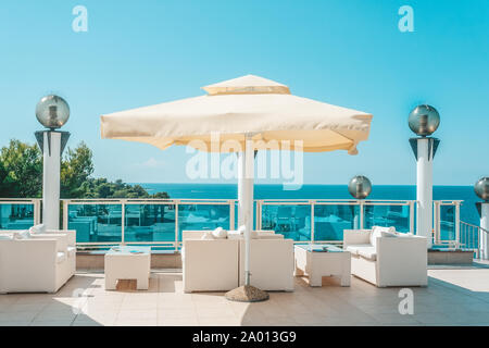 Grand parapluie blanc et de meubles de jardin sofas et chaises en rotin avec coussins et une table en verre. Pour se détendre sur la terrasse de l'hôtel Banque D'Images