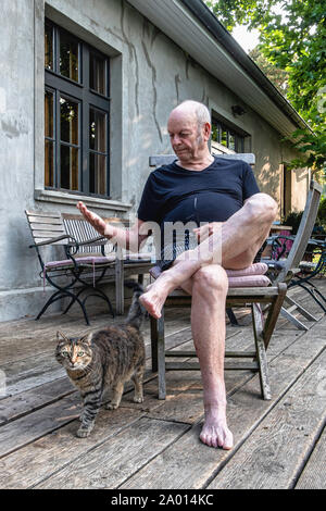 Un homme âgé et chat tigré sur terrasse en bois de ferme à Pinnow, Uckermark,Brandenburg, Allemagne Banque D'Images