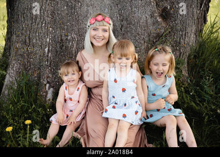 La qualité de mère ayant le temps de jeu drôle avec son bébé filles à un parc blowing dandelion - Jeune blonde - hippie filles porter des robes similaires avec Banque D'Images