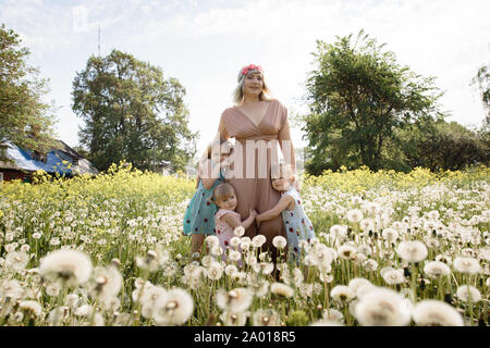 La qualité de mère ayant le temps de jeu drôle avec son bébé filles à un parc blowing dandelion - Jeune blonde - hippie filles porter des robes similaires avec Banque D'Images