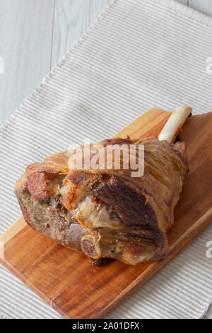 Gigot d'agneau rôti en appui sur une planche à découper en bois et set de table. Fond en bois gris Banque D'Images