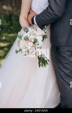 Close up de la mariée dans une robe blanche et un groom dans un costume en l'embrassant, et ils ont prévu un magnifique bouquet de fleurs blanches, roses et de la verdure, décoré. Banque D'Images