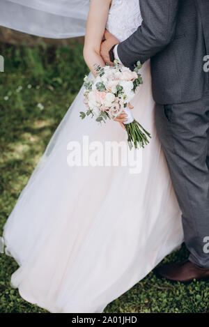 Close up de la mariée dans une robe blanche et un groom dans un costume en l'embrassant, et ils ont prévu un magnifique bouquet de fleurs blanches, roses et de la verdure, décoré. Banque D'Images