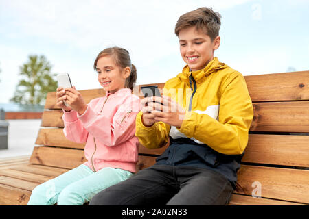 Les enfants avec les smartphones assis sur banc de la rue Banque D'Images