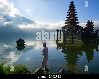 Petit matin tranquille près du lac avec temple balinais et non reconnu avec jeune homme costume balinais au Lac Batur à Kintamani Bali Indonesia. Banque D'Images