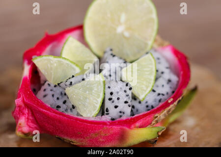 Fruits du dragon tranchés et citron vert tranchés dans une bande de jus de fruit du dragon pelé sur un fond de table en bois ancien. Banque D'Images