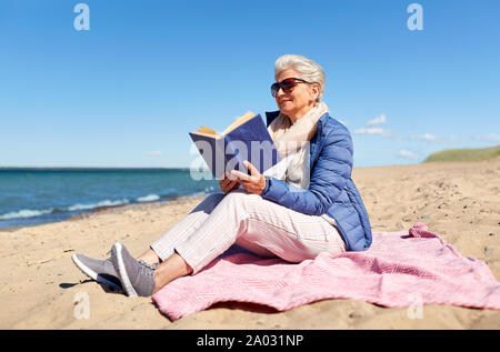 Happy senior woman reading book on été plage Banque D'Images