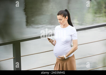 Jeune femme en habits de marcher le long du pont et de la lecture d'un message sur son téléphone portable Banque D'Images