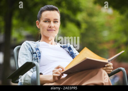 Portrait of young woman relaxing on chaise avec réserve et à la recherche à l'extérieur de l'appareil photo Banque D'Images