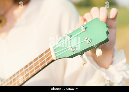 Cordes ukulele tuning femme. Le manche de l'instrument de musique est couleur menthe. Des tons de vert à la mode Banque D'Images