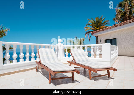 Transats sur la terrasse avec vue océan et villa palm tree background Banque D'Images