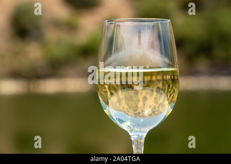 Verre de vin blanc sur un bateau de croisière sur le fleuve Douro au Portugal reflète la rivière et les vignobles bordant la rivière Banque D'Images