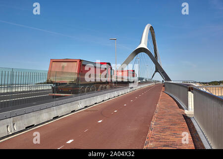 De couleur rouge, deux camions à benne basculante roulant sur le pont de passerelle d'un pont bowstring nommé De Oversteek qui enjambe la rivière Waal à Nimègue Banque D'Images