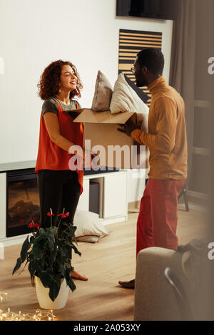 Femme excitée. Type de peau foncée man holding box tout en aidant son partenaire Banque D'Images