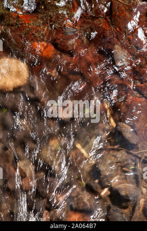 Résumé de l'eau courante, rouge, de roches riches en fer en vertu de l'eau brillant Banque D'Images
