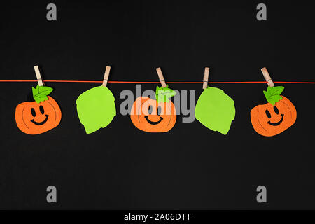 Arrière-plan de thème de l'halloween décorations. Citrouilles jouet suspendu à une chaîne avec le cas des pinces à linge en bois sur fond noir. Copier l'espace. Mise à plat de style. Banque D'Images