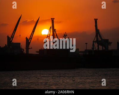 Kaohsiung, Taiwan : silhouette noire de navires porte-conteneurs et de grues à Kaohsiung port industriel au coucher du soleil avec orange ciel nuageux Banque D'Images