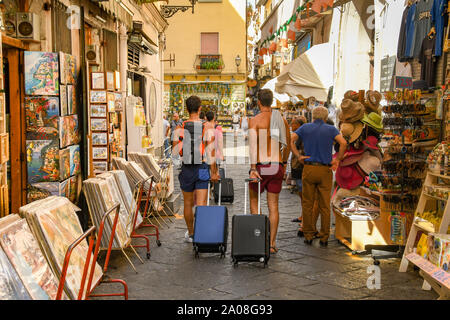 SORRENTO, ITALIE - AOÛT 2019 : jeunes tirant valises passé boutiques de souvenirs dans la vieille ville de Sorrento. Banque D'Images