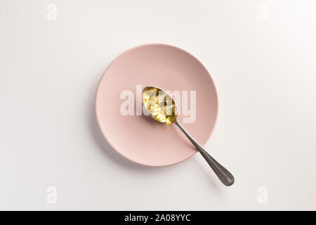 Cuillère avec des capsules d'huile de poisson, sur la plaque. Mise à plat. Banque D'Images