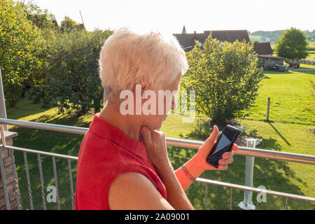 Hauts femme essayant de lire un message au soleil sur un téléphone cellulaire Banque D'Images