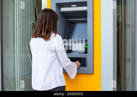 Vue arrière d'une jeune femme à l'aide d'un guichet automatique pour retirer ou transférer de l'argent Banque D'Images