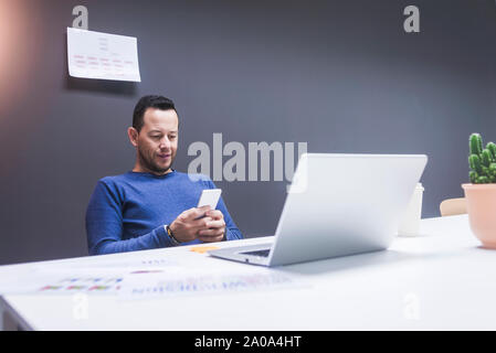 Jeune homme lisant son smartphone. Portrait of business man reading message avec smartphone dans Office. L'homme travaillant à son bureau au bureau. Banque D'Images
