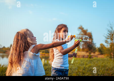 Pour souffler des bulles de savon en parc d'été par la rivière. Les enfants se battent pour essayer de faire éclater la bulle. Dispute entre soeurs Banque D'Images