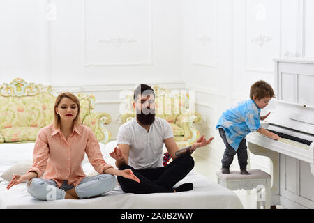 Les jeunes parents de méditer, tandis que leur petit-fils à jouer du piano, les parents. Exercices de yoga en couple ne lit. Kid ennuyé les parents avec le bruit. Maman Banque D'Images