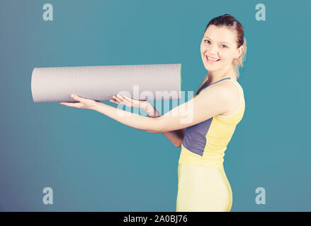 Cours de concept. La pratique du yoga tous les jours. Girl smiling slim fit tapis de sol fitness hold de l'athlète. Remise en forme et stretching. L'étirement des muscles. Entrer dans la rainure de yoga. Le yoga comme passe-temps et le sport. Banque D'Images