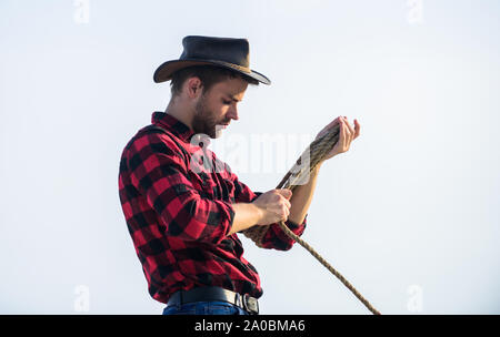 Ranch travailleur. Eco farm. La vie au ranch. Cowboy avec lasso corde fond de ciel. Concept de l'agriculture. Bel homme en chapeau et costume de style rustique. Garder ranch. Agriculteur réfléchie réflexion sur l'entreprise. Banque D'Images