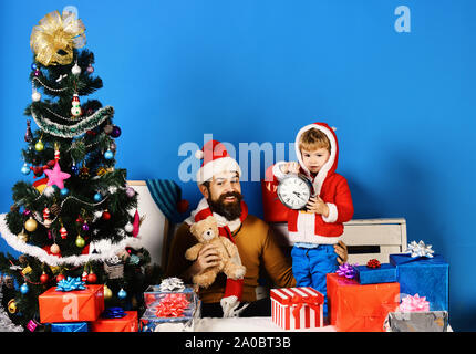 Le Père Noël et petit elfe tenir vieille horloge montrant cinq à minuit. Attend de la famille pour le Nouvel An sur fond bleu. Garçon et l'homme avec de la barbe et de visages heureux de célébrer Noël. La veille de Noël et le concept de temps Banque D'Images