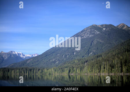 Ciel bleu et vert de l'été à Birkenhead Lake montagnes reflétant avec la lune qui brille au-dessus de la lumière du jour Banque D'Images