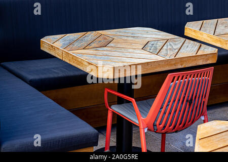 Une table en bois en plein air sur un restaurant patio est entouré d'un tissu et une chaise en plastique rouge. Banque D'Images